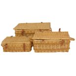 A graduated set of three wicker hampers, with brown leather straps, the largest 77cm wide.