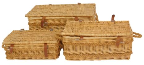 A graduated set of three wicker hampers, with brown leather straps, the largest 77cm wide.