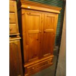 A pine two door wardrobe, with a single drawer on a plinth.