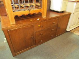 An oak low sideboard, with an arrangement of two cupboard doors and three drawers.