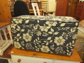 An ottoman storage basket, decorated in black floral print. The upholstery in this lot does not