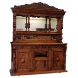 A late 19thC oak sideboard, the raised top with a leaf carved frieze above a two bevelled mirror pla