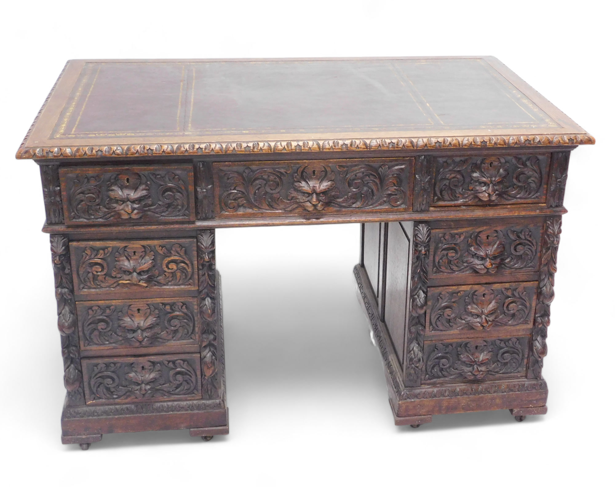 A late Victorian oak pedestal desk, carved with scrolls, leaves and masks, the rectangular top with