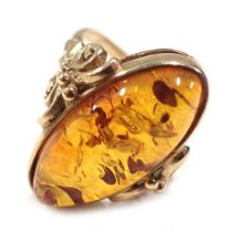 A 9ct gold and amber dress ring, the oval amber in rub over setting, with scroll shoulders, ring siz