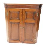 A 19thC oak and mahogany cross banded corner cabinet, with moulded cornice above two panelled doors,