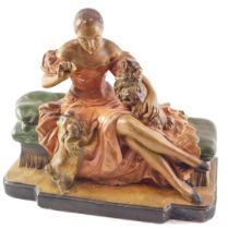 An early 20thC painted chalkware figure group, modelled in the form of a lady seated on a day bed be