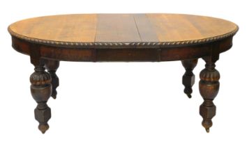 An early 20thC oak extending dining table, the oval top with a gadrooned border on bulbous cup and c