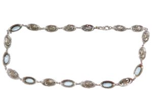 A 1960s/70s necklace, set with blue paste stones in oval white metal links, with scroll decoration,