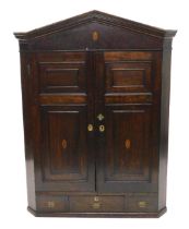 A early 19thC oak and mahogany corner cabinet, the arched cornice above two panelled doors, each lat
