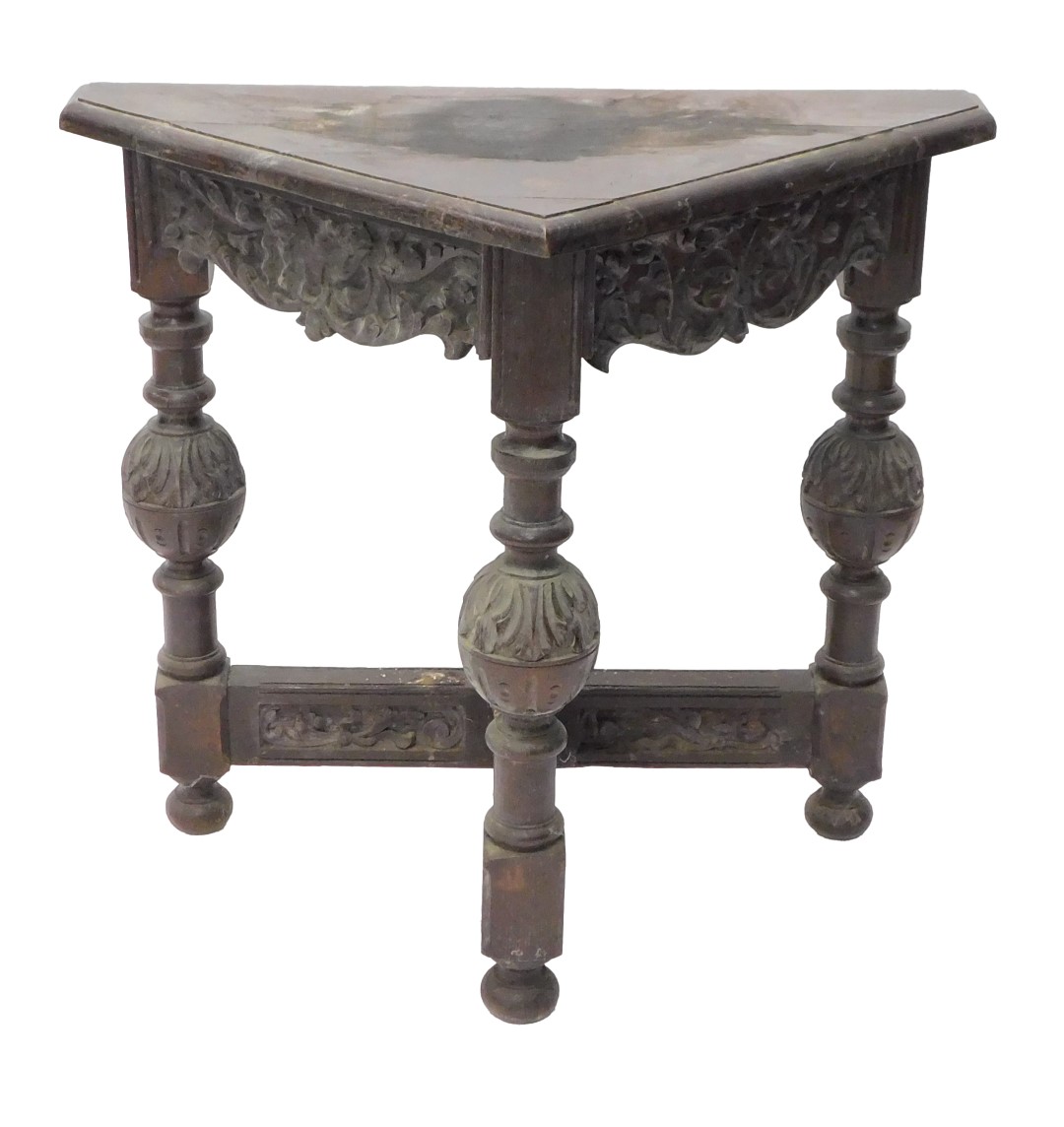 A carved oak triangular side table, the frieze decorated with scrolls, on cup and cover leaf carved