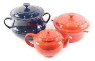 A Le Crueset blue stoneware casserole dish and cover, another similar in red, and a teapot. Buyer N