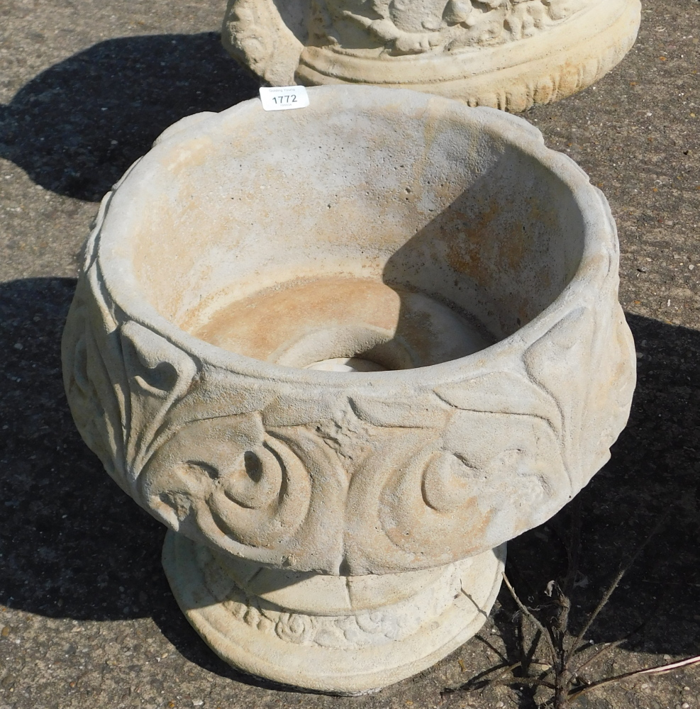 A reconstituted stone fleur de lys pattern urn, stylised with three petal design, on a circular foot