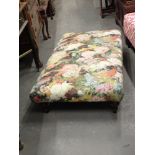 A long footstool, upholstered in floral transfer print, on mahogany legs.