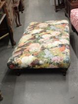 A long footstool, upholstered in floral transfer print, on mahogany legs.