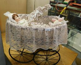 A wrought metal doll's pram, with linen throws and doll.