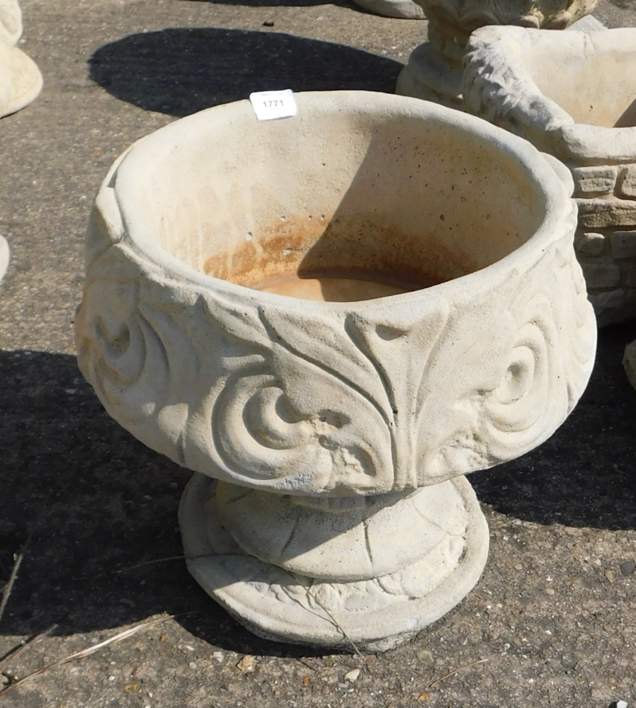 A reconstituted stone fleur de lys pattern urn, stylised with three petal design, on a circular foot