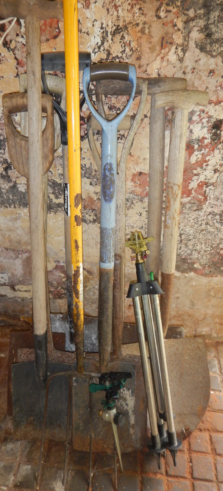 A collection of spades, shovel, hay fork and two garden sprinklers.