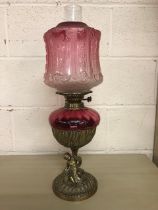 Antique Victorian cranberry glass oil lamp with brass cherub base approximately 57cm high