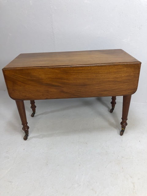 Pembroke table in flame mahogany on turned legs on casters, drawers to either end