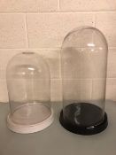 Glass display Domes, one approximately 50cm x 24cm with black ceramic base, and one approximately 38