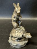 A circa 1920 Henri Payne mascot depicting a hare with arm in bandage upon a tortoise.