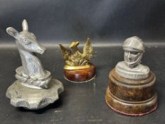 Three car accessory mascots: a Whitbread Brewery doe head on radiator cap, Phoenix Assurance in