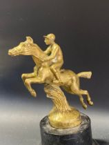 A polished brass car accessory mascot depicting a jockey on a leaping horse, by repute by A.E.