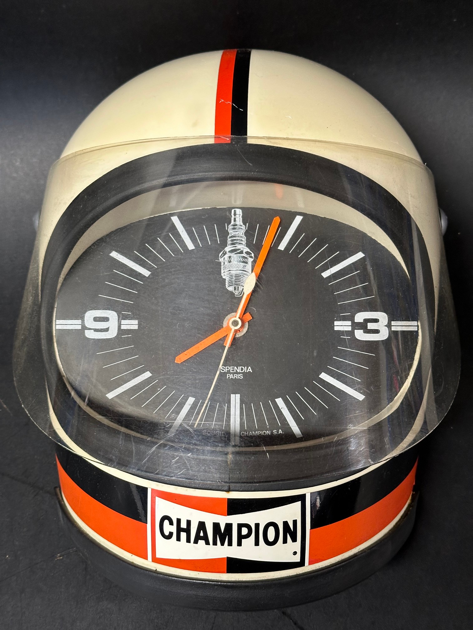 A Champion Spark Plugs advertising wall clock in the form of a racing driver's helmet, battery