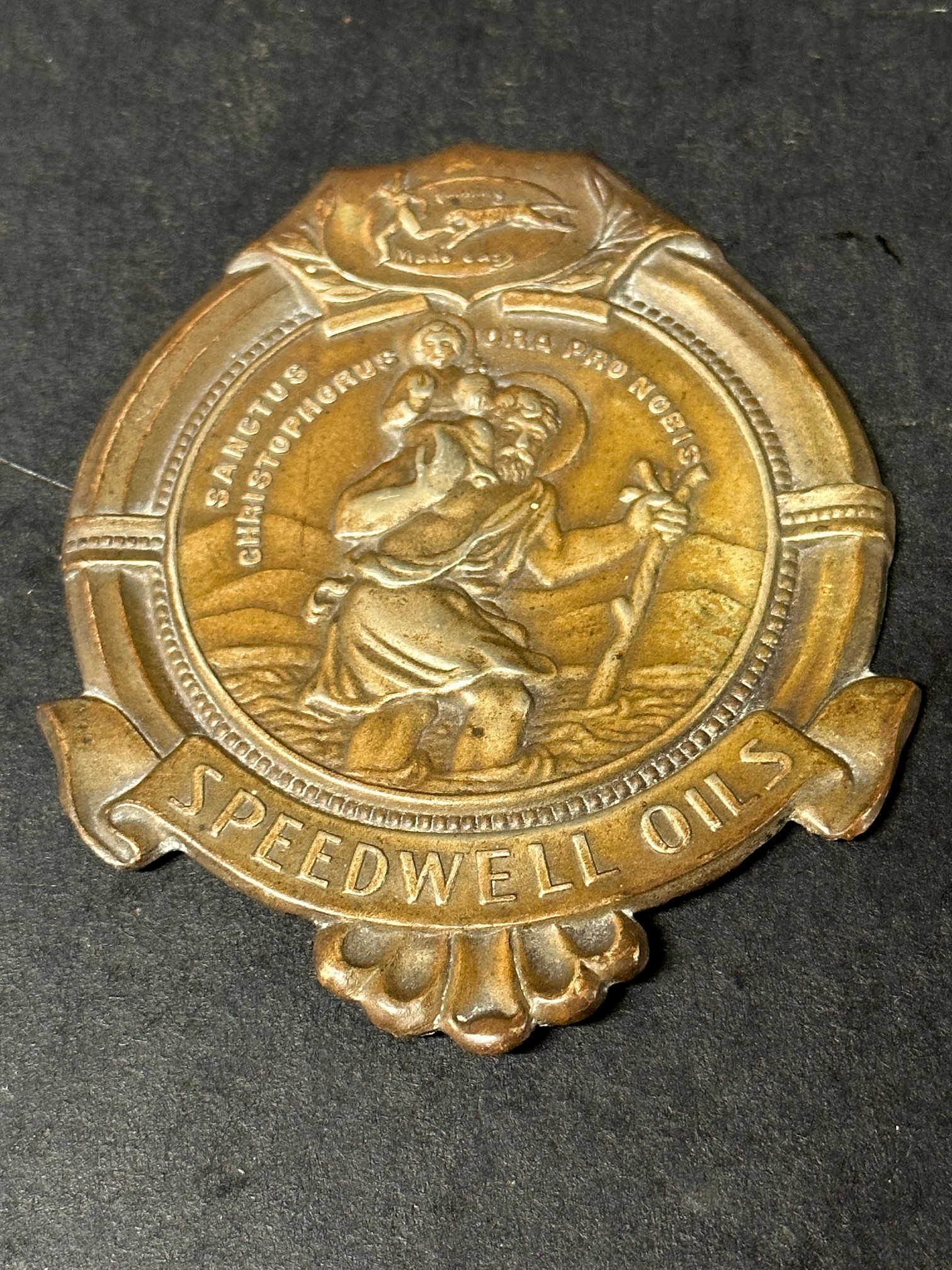 A St. Christopher dashboard plaque (patron saint for safe travel) advertising Speedwell Oils.