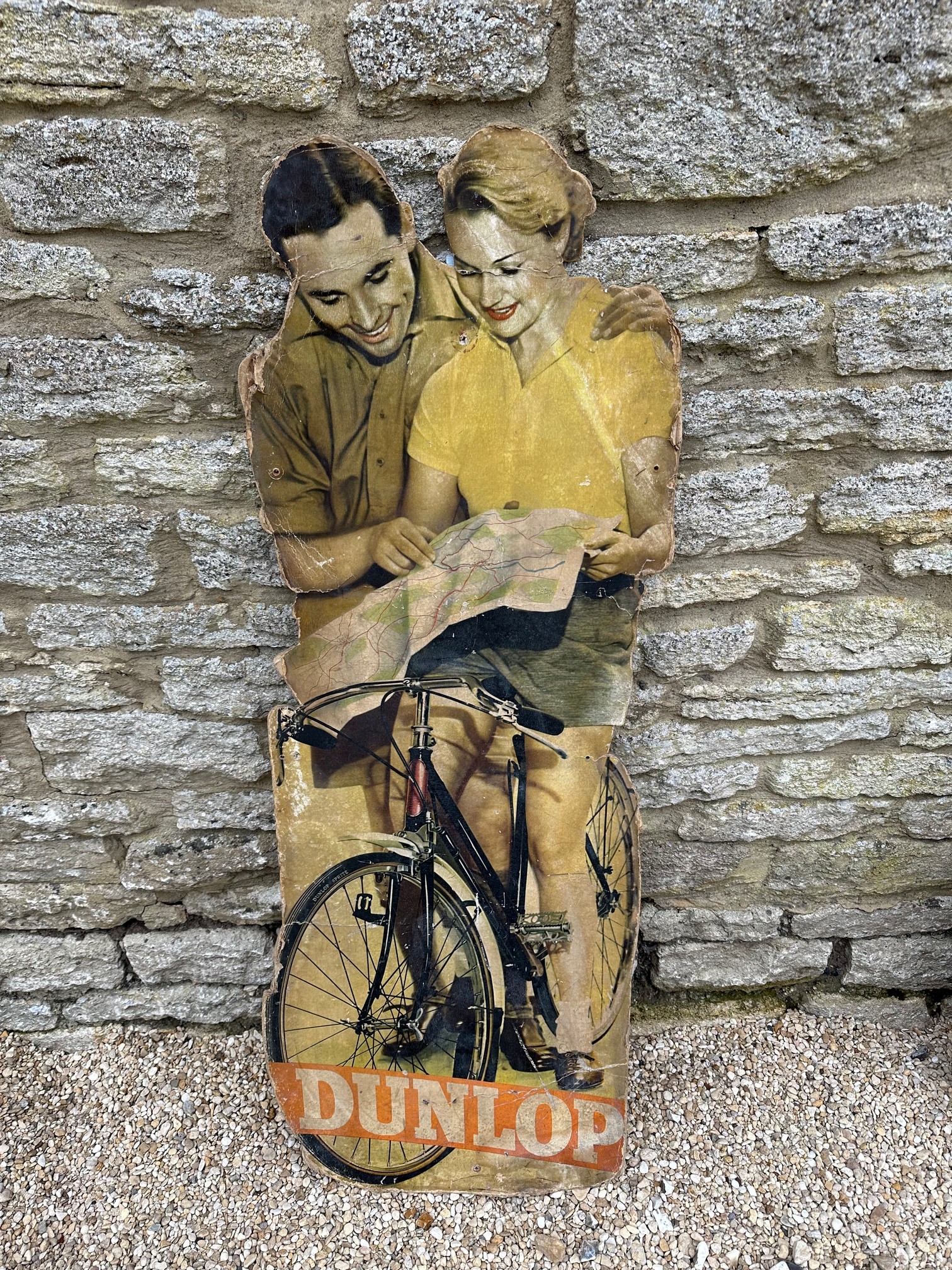 A rare Dunlop Cycle showcard depicting a couple reading a map, the lady perched on a bicycle with