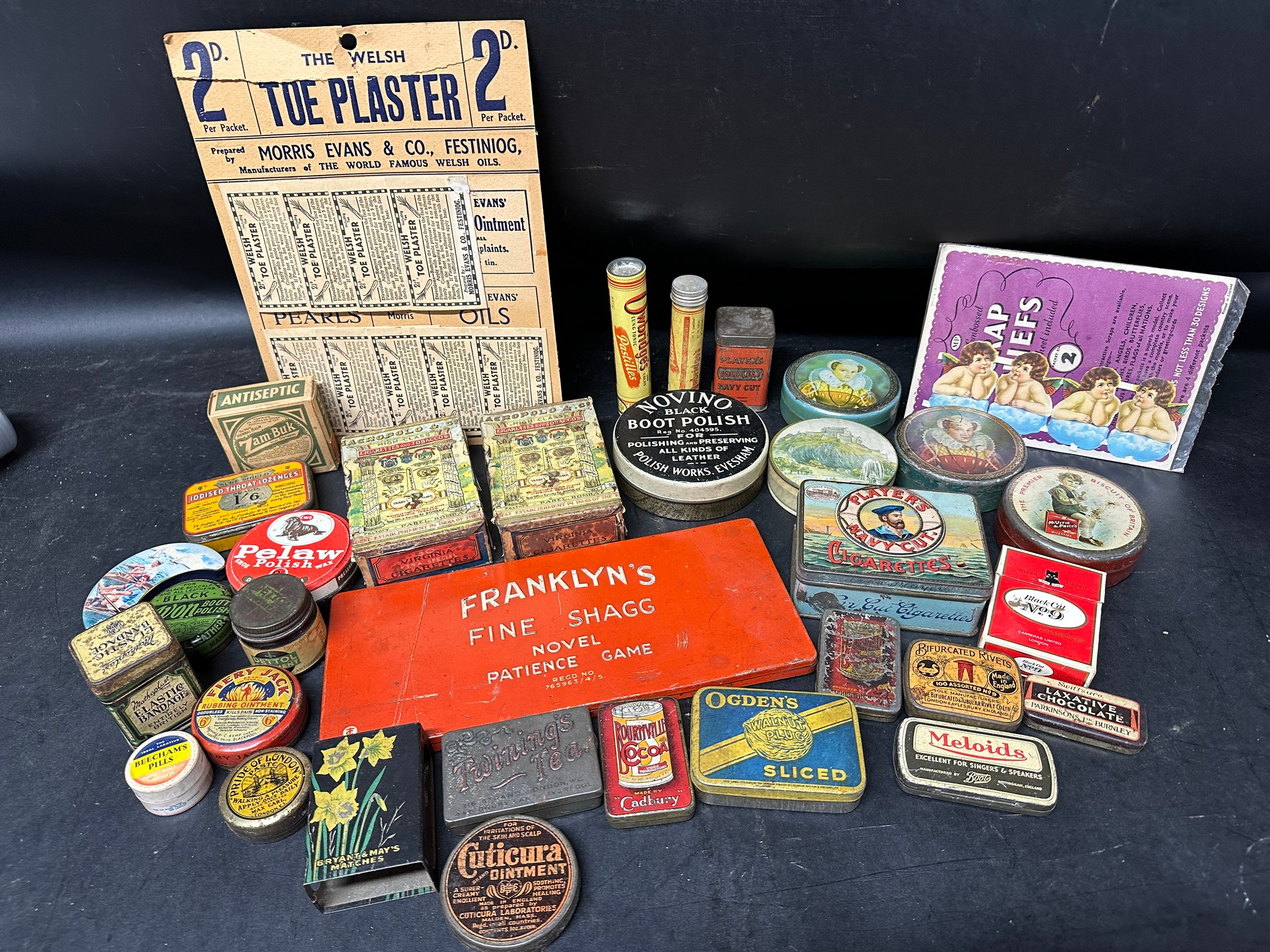 A selection of tins, a match case, a Franklyn's Fine Shagg novel patience game, toe plaster point of