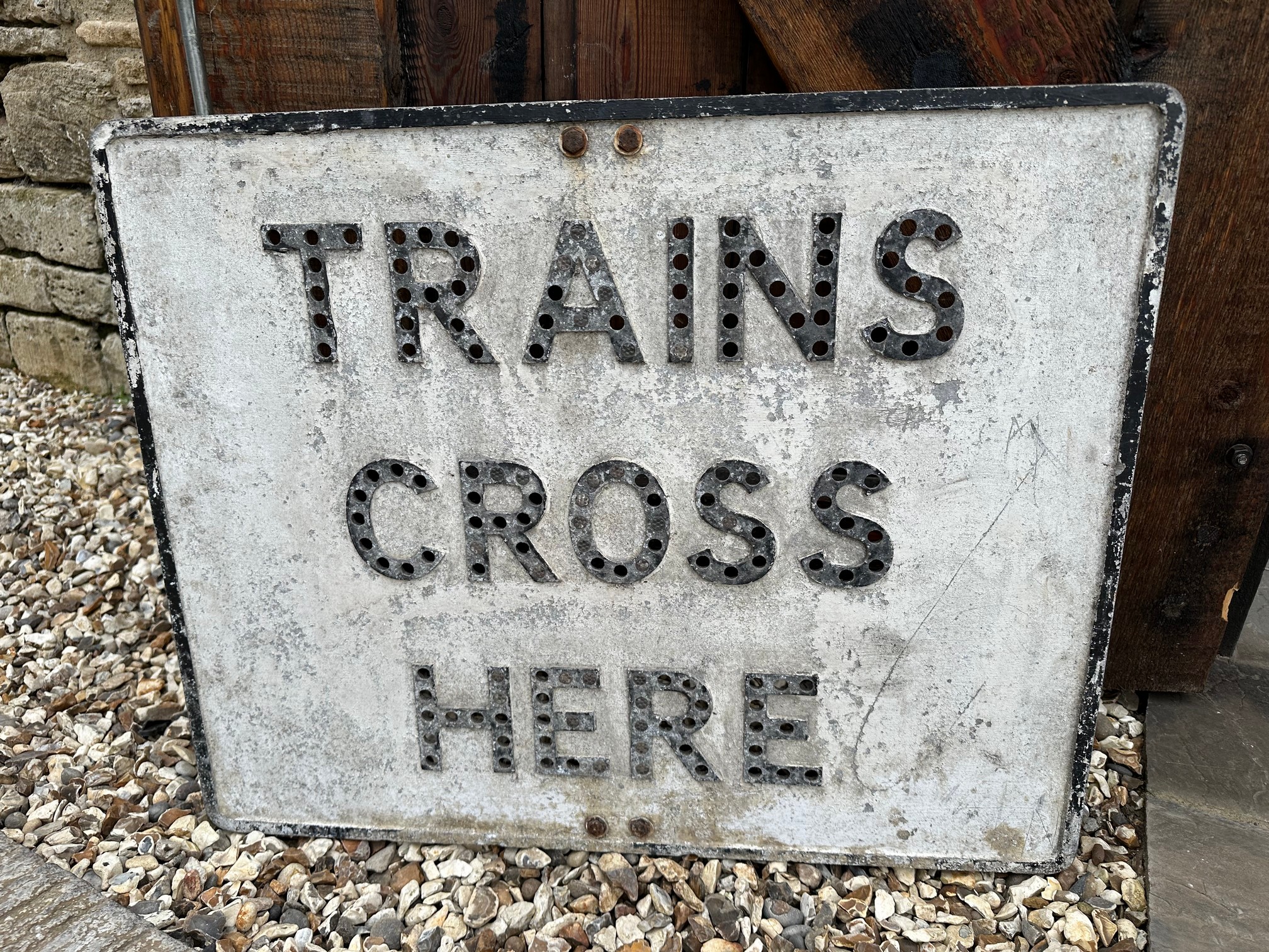 Trains Cross Here - a cast aluminium road sign with pole mounts, some glass reflector beads present,