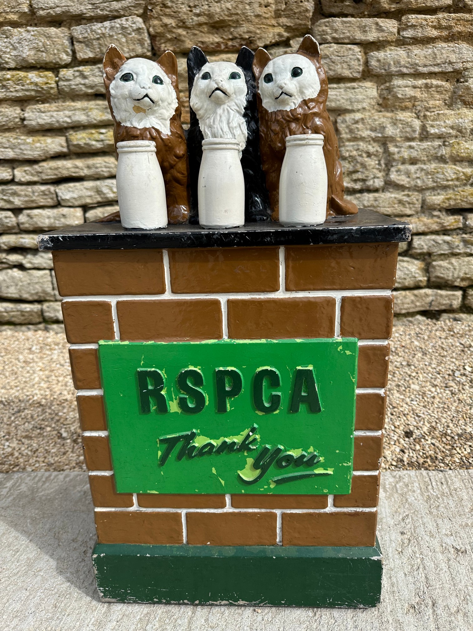 An RSPCA charity donation box with three cats upon a wall behind three milk bottles, with carry