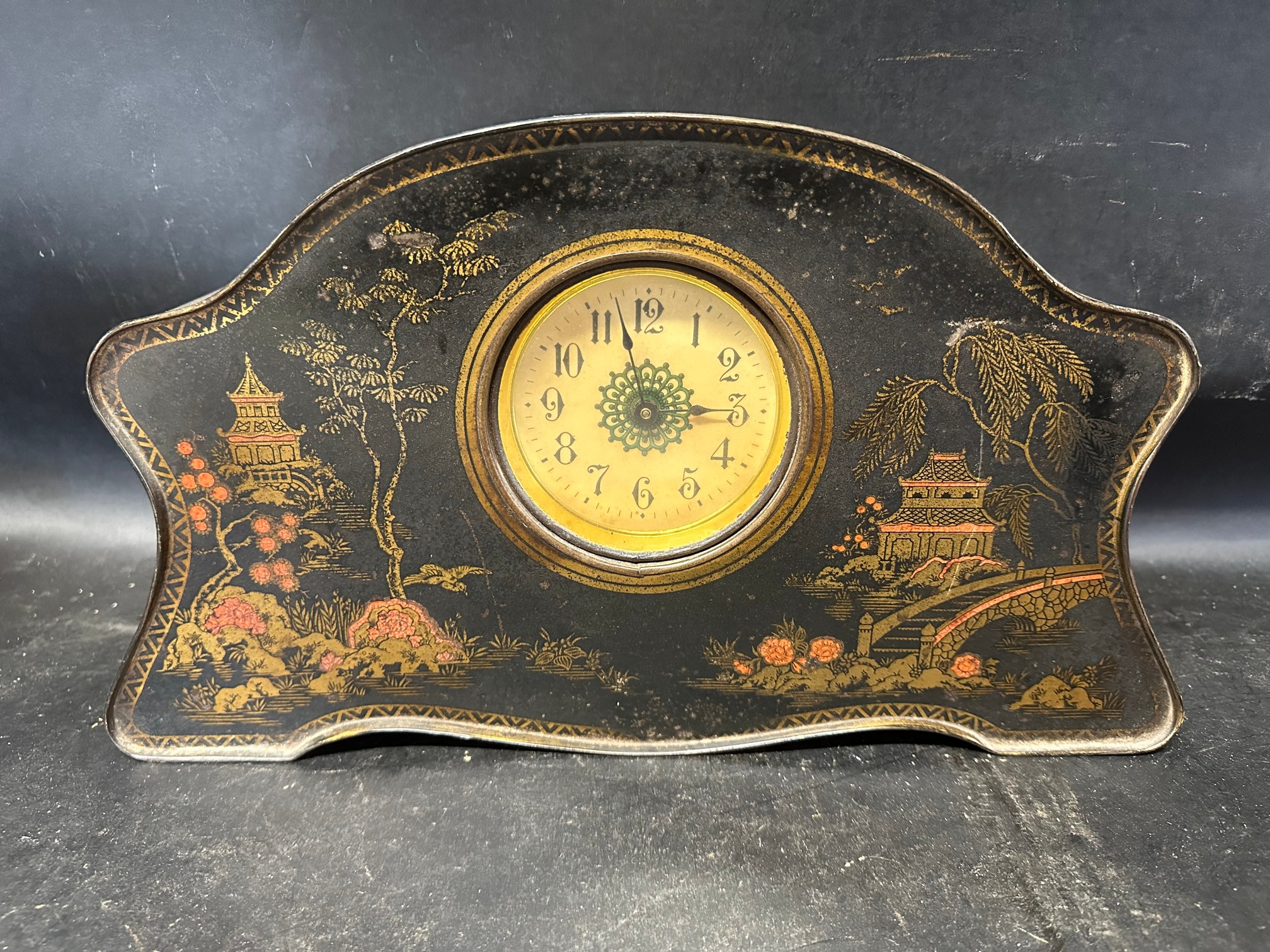 A shaped tole clock confectionery tin circa 1910 depicting Oriental scenes, possibly by Champion