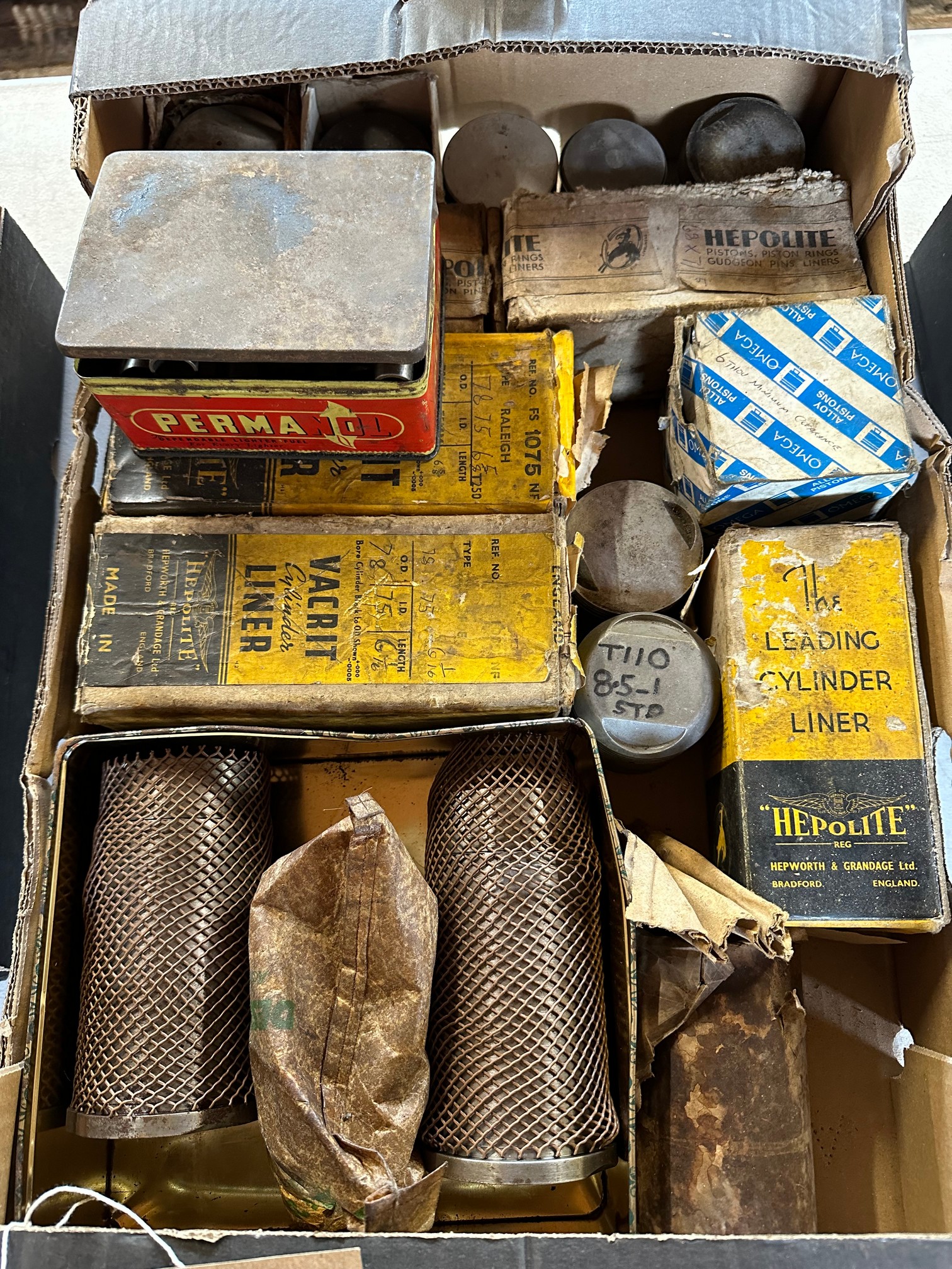 A box of cylinder liners (appear new old stock), pistons and gudgeon pins.