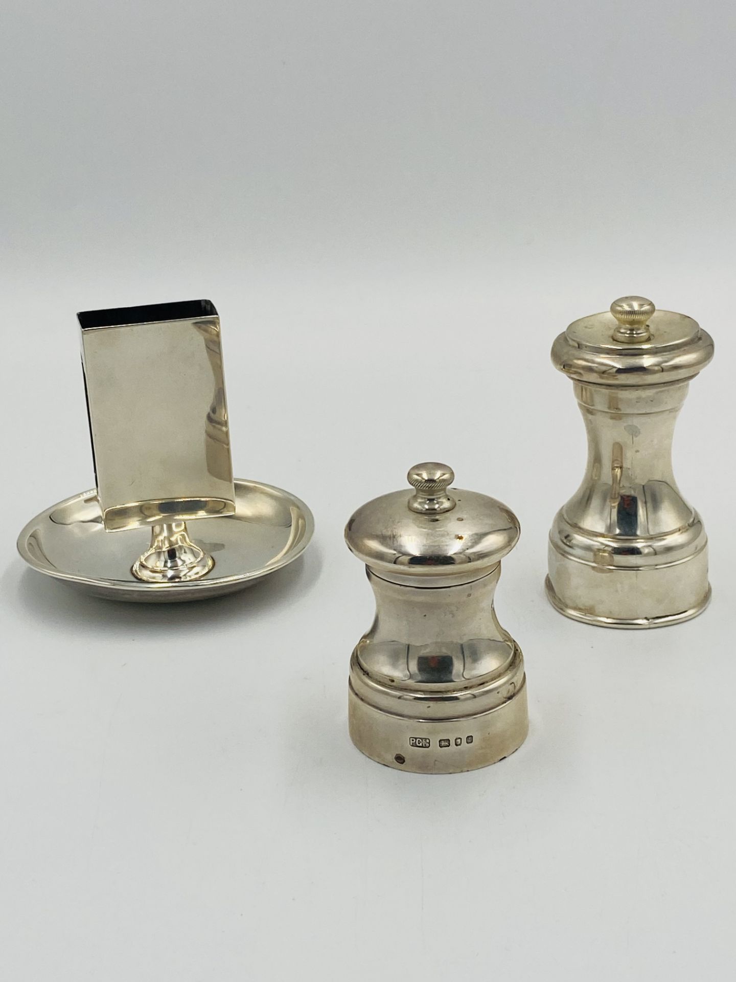 Two silver pepper grinders together with a silver matchbox holder