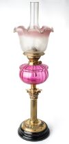 A Victorian oil lamp with a black porcelain base with brass fittings and fluted cranberry glass