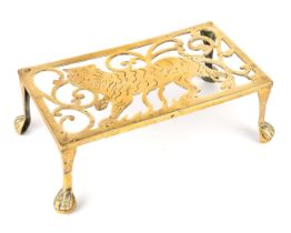 A 19th century rectangular brass trivet, depicting a tiger, raised on four legs with paw feet,