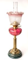 A Victorian oil lamp with majolica base with brass fittings and enamelled cranberry glass body.