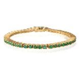 A yellow metal and emerald line bracelet, set with round-cut emeralds in prong settings, box clasp