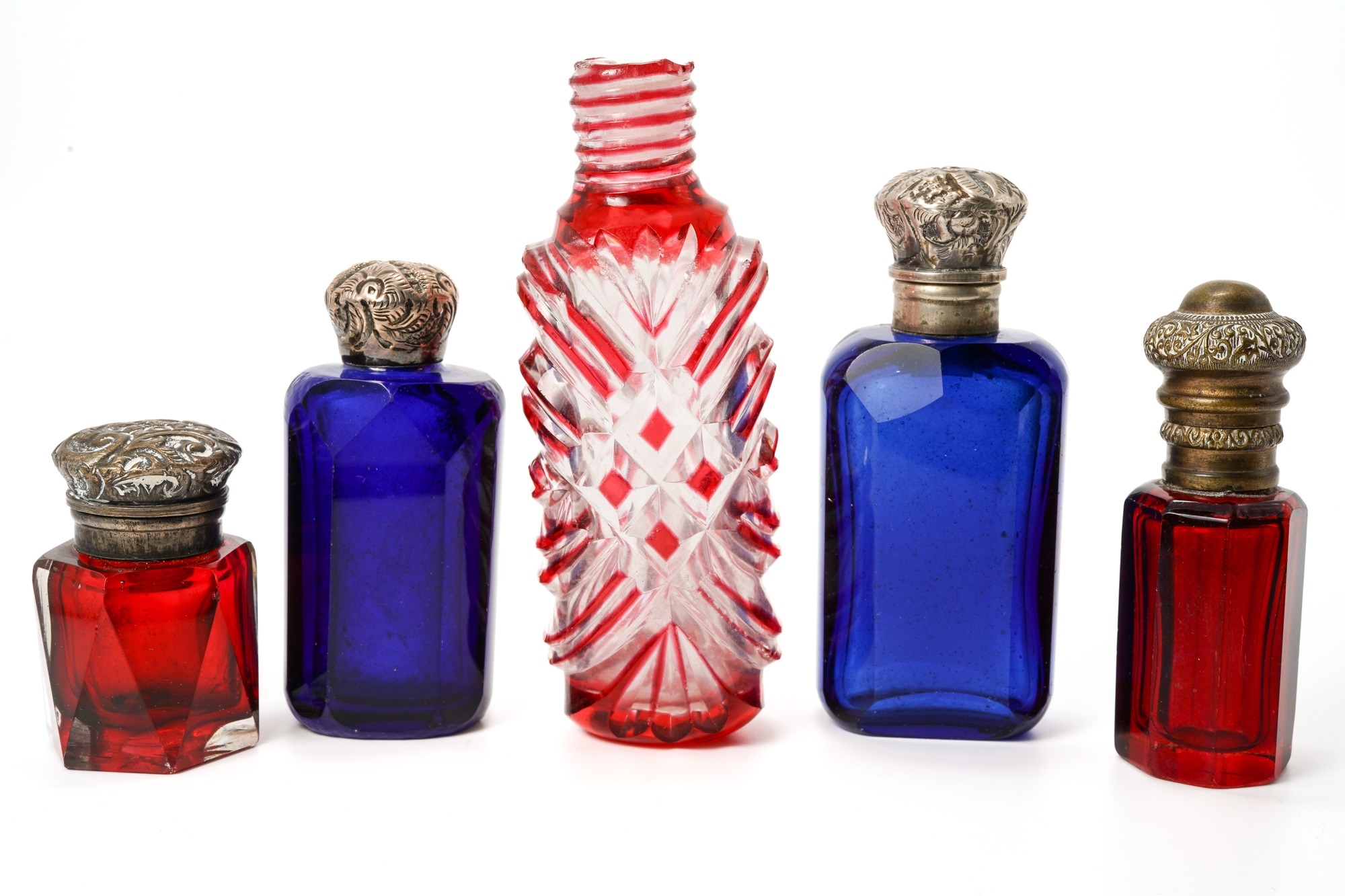 A collection of five red and blue glass scent bottles, two with silver lids, two with base metal