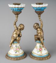 A pair of decorative metal and earthenware candlesticks, each cast as a putto holding scones
