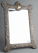 A large Edwardian silver mounted shaped rectangular easel mirror, the embossed and pierced foliate