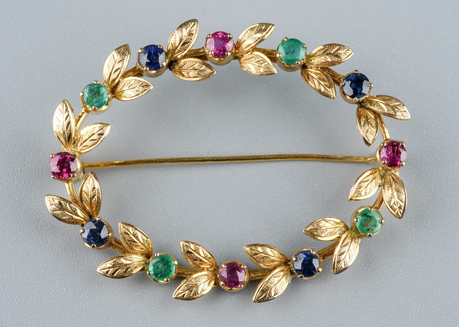 A yellow gold and gem-set oval brooch, set with rubies, emeralds and sapphires, approx 4.5cm wide,