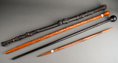 A blackened naturalistic wood Shillelagh style stick together with two carved staffs and a carved