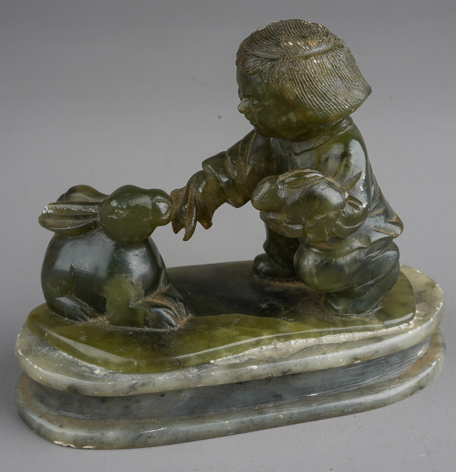 A nephrite coloured carved figure of boy holding a rabbits on an oval plinth base damage to larger