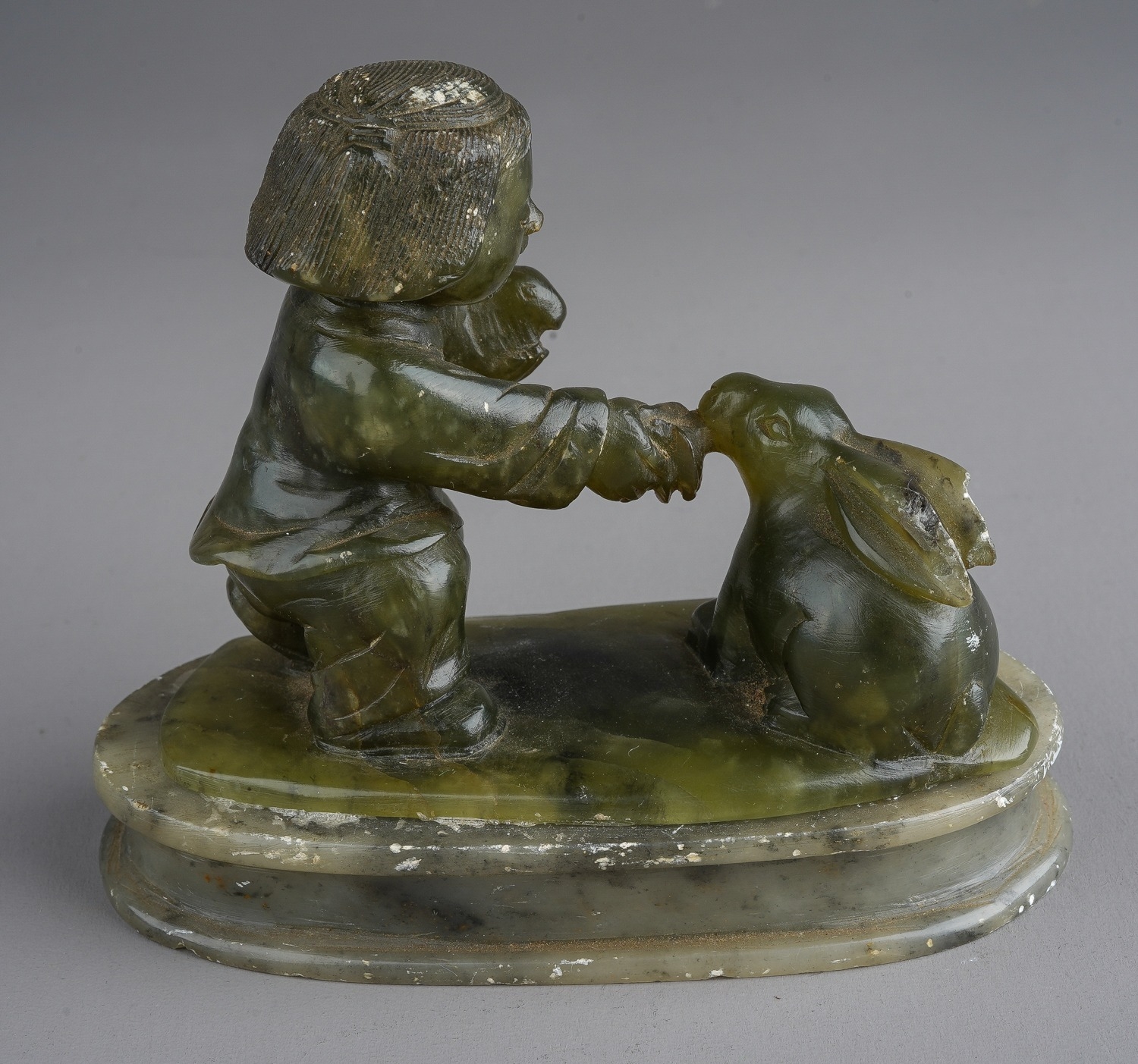 A nephrite coloured carved figure of boy holding a rabbits on an oval plinth base - Image 2 of 2