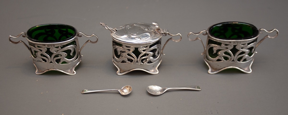 An Art Nouveau style silver condiment set to include mustard pot with cover and a pair of two