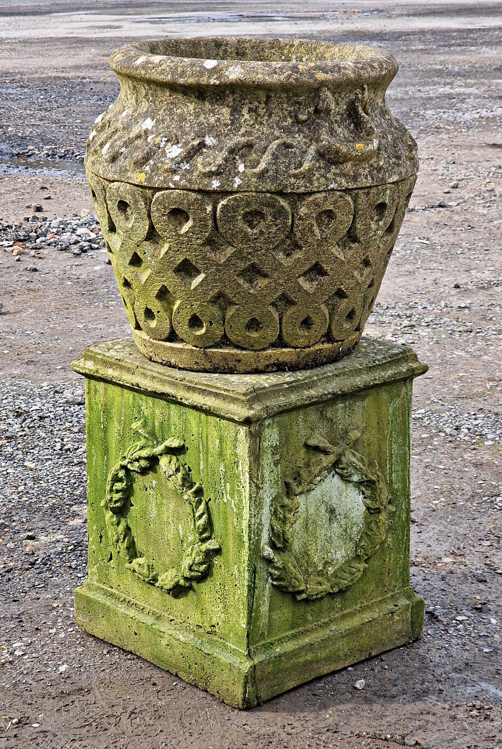 A weathered reconstituted stone garden planter with repeating lattice detail raised on a square