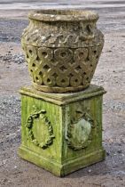 A weathered reconstituted stone garden planter with repeating lattice detail raised on a square